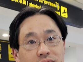 Michiharu Hyogo: Citizen Scientist Leads New NASA Study A man with short black hair, glasses, and a neutral expression is standing in an airport terminal. Yellow signage with directional symbols is visible in the background.
