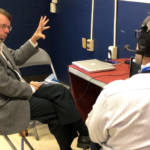 Keith Koehler: Wallops’ News Chief Excels in Leadership and Communication Keith Koehler, a white man with short brown hair and beard, sits in a chair and gestures with one hand while doing a radio interview. He wears headphones, a taupe jacket, and dark pants.