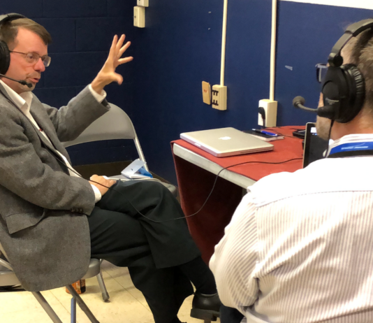 Keith Koehler: Wallops’ News Chief Excels in Leadership and Communication Keith Koehler, a white man with short brown hair and beard, sits in a chair and gestures with one hand while doing a radio interview. He wears headphones, a taupe jacket, and dark pants.