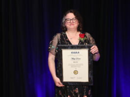 Misty Davies Named 2024 AIAA Fellow by NASA Misty Davies holding a framed AIAA Fellowship certificate with a red rose on her lapel, standing against a dark background.