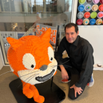 Mark SubbaRao Transforms NASA Data into Artistic Creations A man with dark hair kneels next to a large LEGO sculpture of an orange and white cartoon cat.