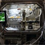 Adam and Hirsa Unveil NASA’s Ring-Sheared Drop Study A silver laboratory structure with wires and controls, connected to two laptops