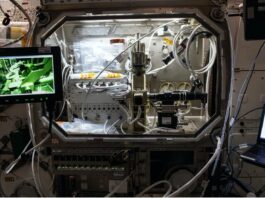 Adam and Hirsa Unveil NASA’s Ring-Sheared Drop Study A silver laboratory structure with wires and controls, connected to two laptops