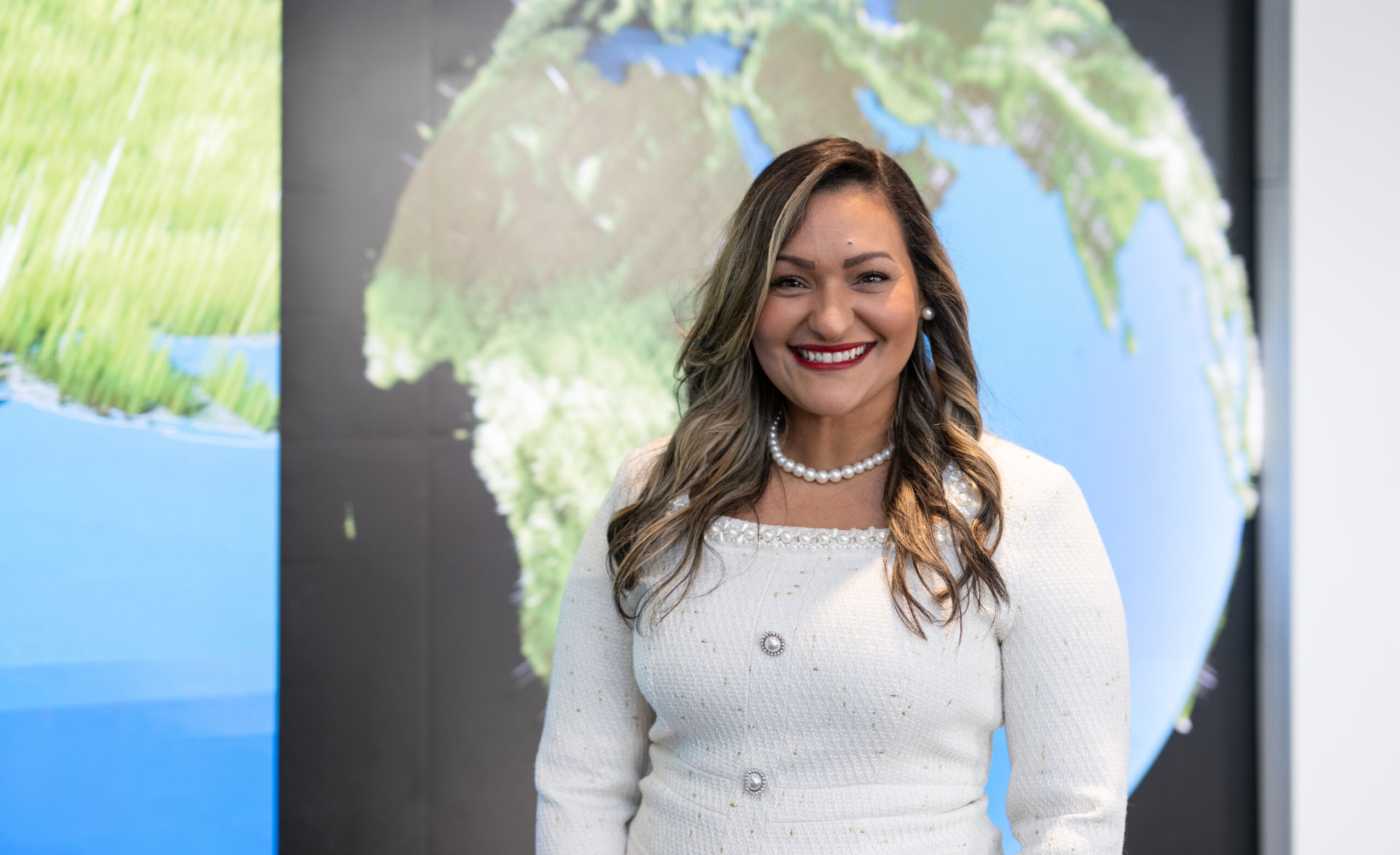 nhq202410030001.jpg Yaíta smiles broadly at the camera wearing a white dress with a pearl necklace. Her hair is long with curls and she