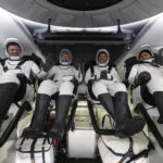 SpaceX Crew-8 Returns to Earth with Florida Splashdown The four NASA SpaceX Crew-8 members sit in a row, smiling and waving in their spacesuits aboard a Dragon spacecraft.