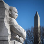 NASA Honors Martin Luther King, Jr. with Memorial A close-up image of a light gray stone statue of Martin Luther King, Jr. in Washington. The Washington Monument is visible in the background, behind the leafless branches of a tree.