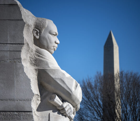 NASA Honors Martin Luther King, Jr. with Memorial A close-up image of a light gray stone statue of Martin Luther King, Jr. in Washington. The Washington Monument is visible in the background, behind the leafless branches of a tree.