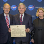 Ex-NASA Astronaut Bob Cabana Honored with Prestigious Civilian Award Nelson, Cabana, and Melroy are side by side, smiling, in front of a background with NASA logos, with Cabana holding the award certificate.