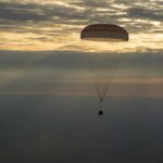 NASA Announces Broadcast for Astronaut Jonny Kim’s Crew Return The photo features a dim horizon with the Soyuz MS-26 spacecraft as it lands by parachute.