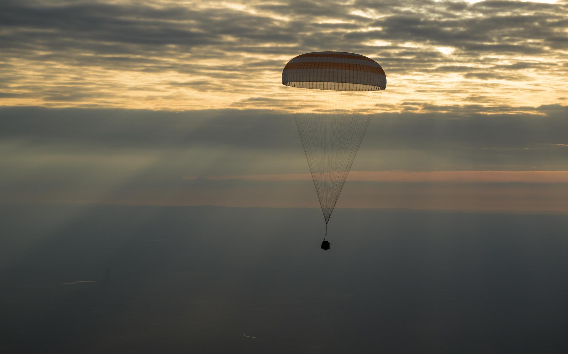 The photo features a dim horizon with the Soyuz MS-26 spacecraft as it lands by parachute.
