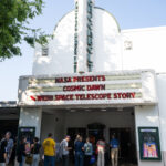Greenbelt Cinema Hosts NASA’s “Cosmic Dawn” Screening Event 10 people stand in a line at a movie theater. About half of the people are standing under the movie marquee, which reads