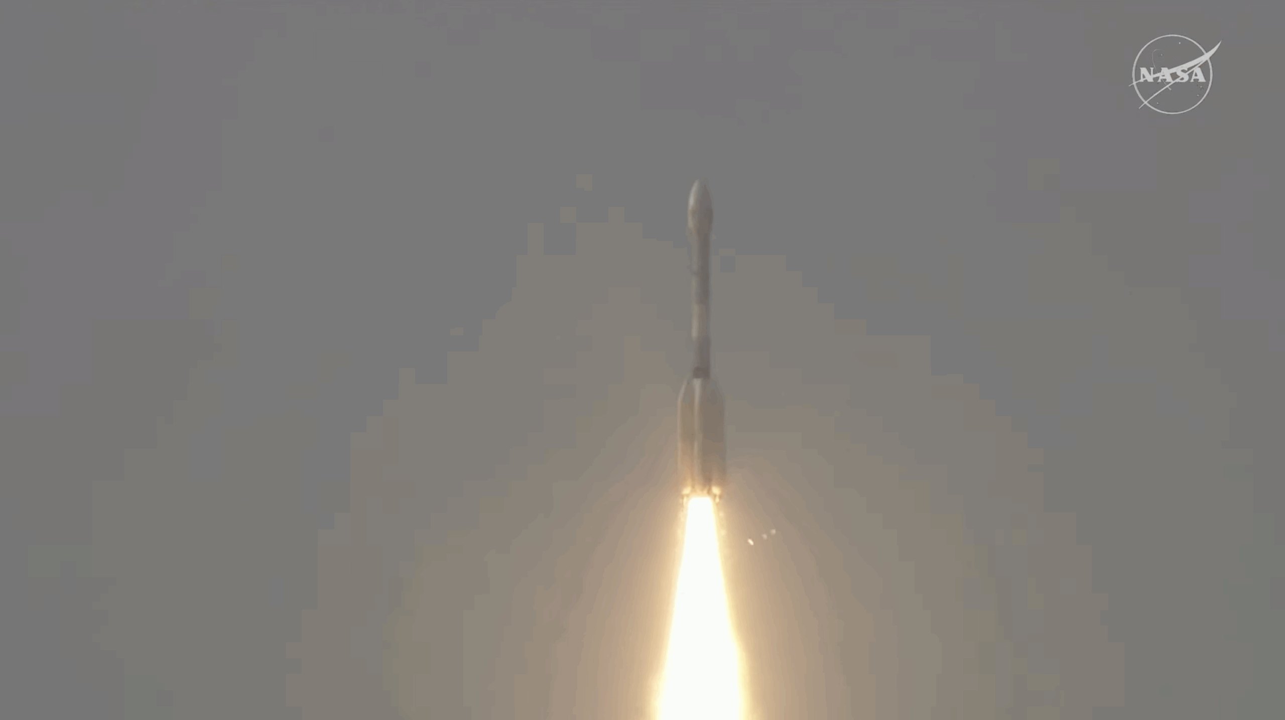 A large white rocket with a fiery trail launches through a cloudy sky above India.