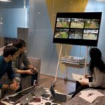 Microsoft Blog: Reaching a New Milestone Three people playing a video game on a large screen.