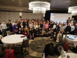 Amateur Scientists Explore Space Life with NASA’s Open Data Large group photo of attendees at a NASA Analysis Working Group meeting, gathered in a conference room with round tables and chandeliers. A presentation screen is visible in the background.