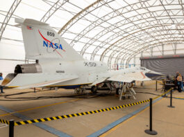 NASA X-59 Achieves Ground-Based Flight Simulation Milestone A white NASA jet airplane sits inside a fabric-covered-roof hangar with several people working at a nearby table with computers.