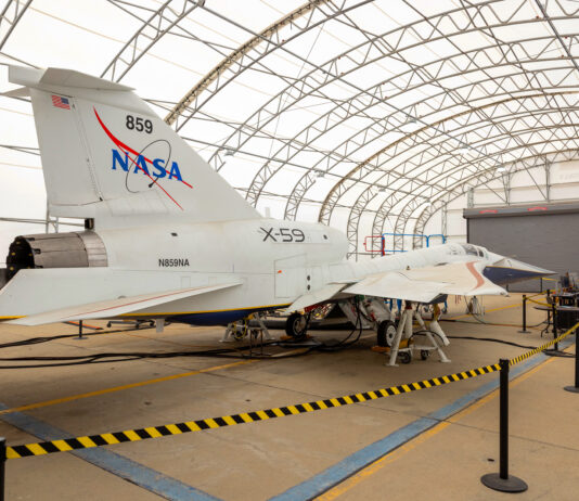 NASA X-59 Achieves Ground-Based Flight Simulation Milestone A white NASA jet airplane sits inside a fabric-covered-roof hangar with several people working at a nearby table with computers.
