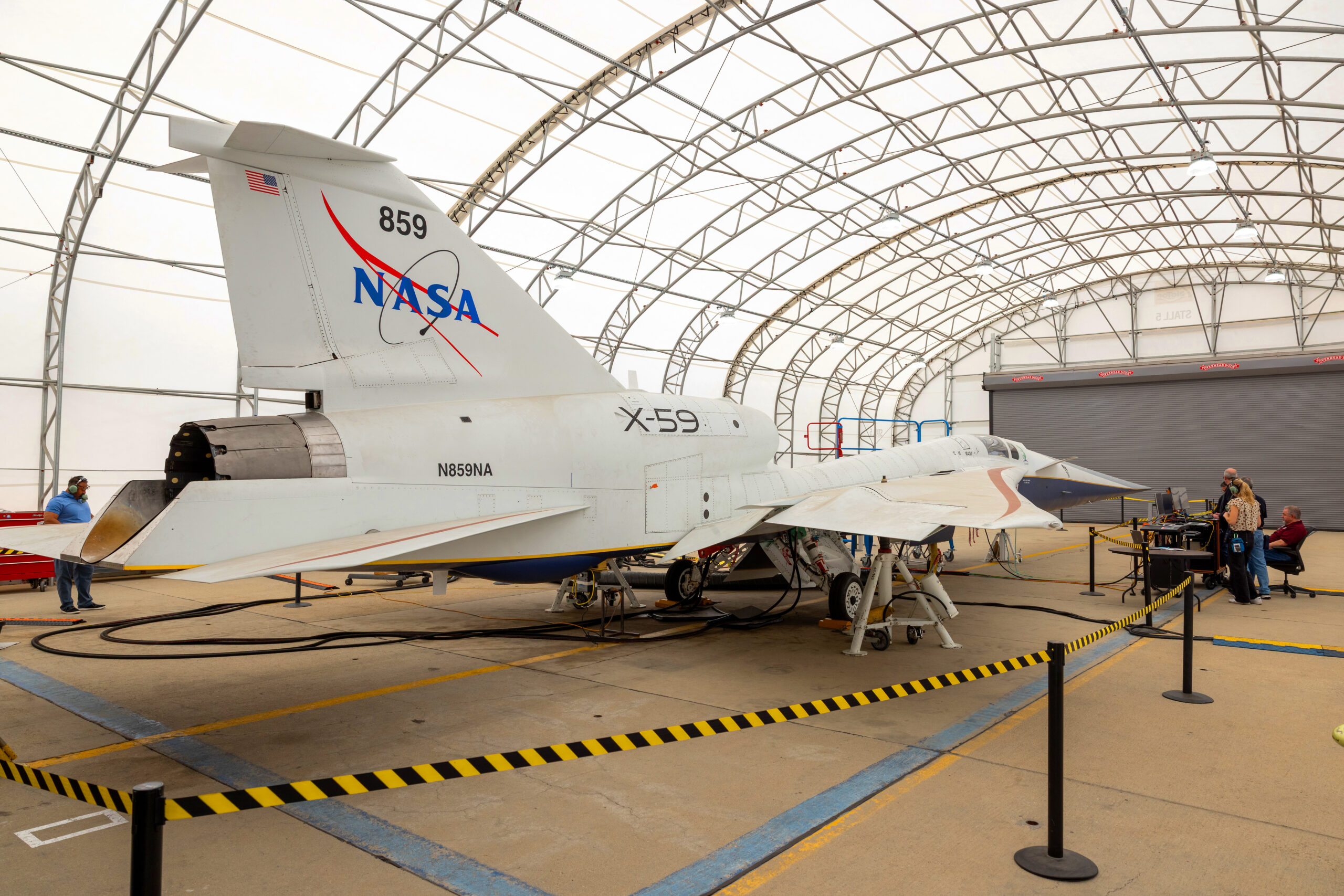 p25 037 35 copy.jpg A white NASA jet airplane sits inside a fabric-covered-roof hangar with several people working at a nearby table with computers.