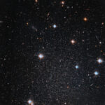 NASA: Hubble Discovers Faint, Star-filled Mini-Galaxy Several stars shine against black space. A few foreground stars with diffraction spikes throughout.