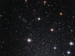 NASA: Hubble Discovers Faint, Star-filled Mini-Galaxy Several stars shine against black space. A few foreground stars with diffraction spikes throughout.