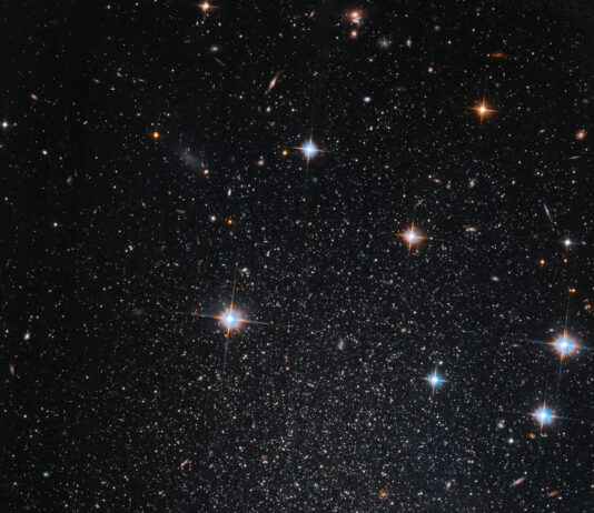 NASA: Hubble Discovers Faint, Star-filled Mini-Galaxy Several stars shine against black space. A few foreground stars with diffraction spikes throughout.