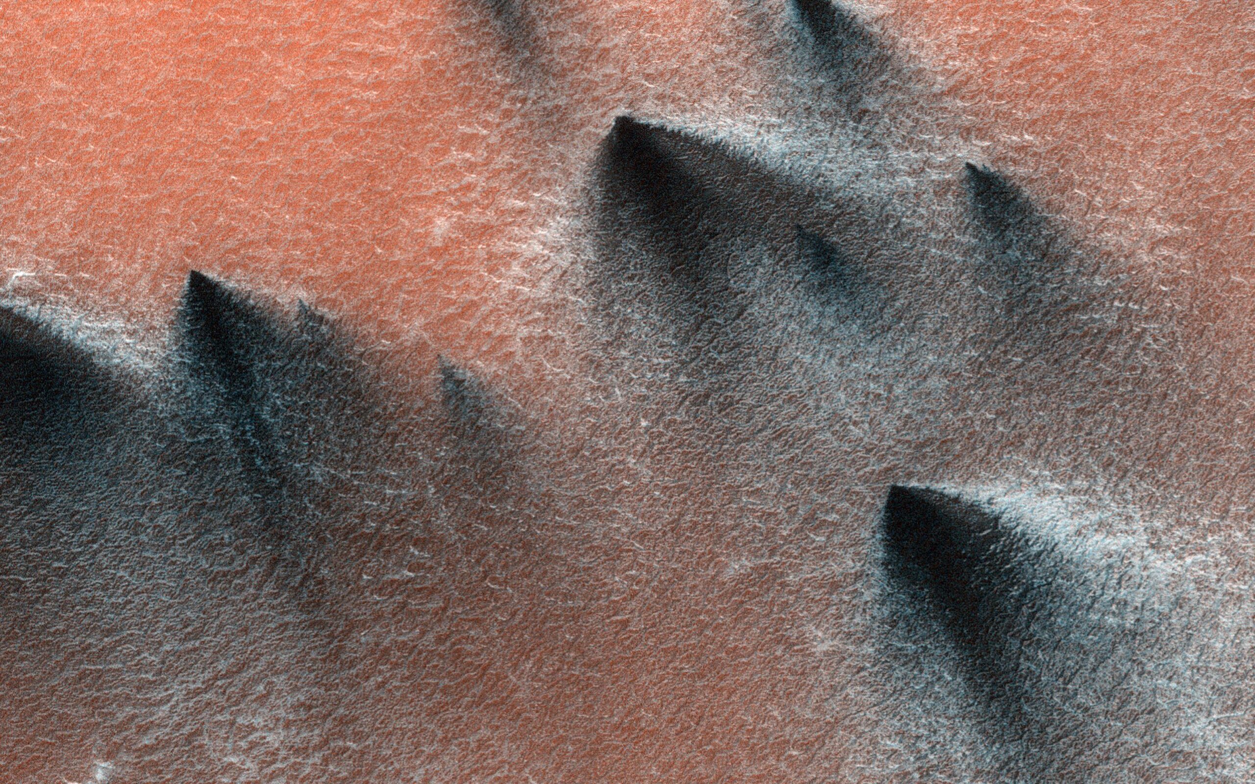 Gas geysers on Mars blow out dark, triangle-shaped fans of dust and sand onto the red Martian surface.
