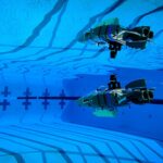 NASA’s Tiny Robot Embarks on Underwater Exploration Mission A small gray plastic robot shaped like a wedge (with propellers and flaps for steering) glides through the blue waters of a competition swimming pool.
