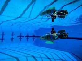 NASA’s Tiny Robot Embarks on Underwater Exploration Mission A small gray plastic robot shaped like a wedge (with propellers and flaps for steering) glides through the blue waters of a competition swimming pool.