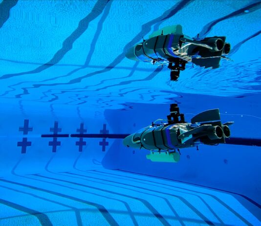 NASA’s Tiny Robot Embarks on Underwater Exploration Mission A small gray plastic robot shaped like a wedge (with propellers and flaps for steering) glides through the blue waters of a competition swimming pool.