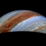 NASA Explores Jupiter’s Chaotic Atmospheric Conditions Part of Jupiter is visible in this image. Its iconic belts and zones stand out in rusty red and blue, along with turbulent activity on their edges.