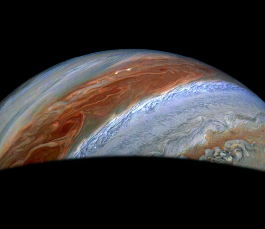 NASA Explores Jupiter’s Chaotic Atmospheric Conditions Part of Jupiter is visible in this image. Its iconic belts and zones stand out in rusty red and blue, along with turbulent activity on their edges.