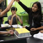 NASA Unveils Free PLANETS Resources for After-School Programs An out of school time educator holds a measuring tape as an elementary aged girl drops a weight to test the space craft shield her group created. Her group members, two boys and one girl, watch as she drops the weight.