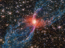 NASA Explores the Mysteries of the Red Spider Nebula A multicolored nebula stands out against the star-studded background of space. The nebula’s central star is hidden by a blotchy pinkish cloud of dust. A strong red light radiates from this area, lighting up the nearby dust. An elongated purple ‘S’ shape is centered on the heart of the nebula, while two blue lobes stretch diagonally outward to the edges of the image, making the entire structure look like a tilted hourglass.