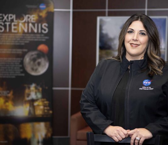 NASA Stennis Celebrates Employee’s Achievement Rebecca Mataya stands for a portrait wearing a black jacket; Stennis posters are shown in the background