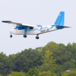 NASA Trials Lightweight Antennas for Future Airspace Advancements A white-and-blue Britten-Norman Defender aircraft outfitted for a flight test with an advanced phased array antenna prototype. The array is mounted on top of the fuselage near the center of the airplane. The plane is seen in flight over trees.