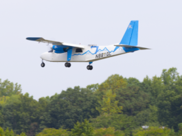 NASA Trials Lightweight Antennas for Future Airspace Advancements A white-and-blue Britten-Norman Defender aircraft outfitted for a flight test with an advanced phased array antenna prototype. The array is mounted on top of the fuselage near the center of the airplane. The plane is seen in flight over trees.