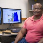 Robert Williams Joins Groundbreaking NASA Project Robert Williams, wearing a coral polo styled shirt, poses for a portrait while seated at his workstation