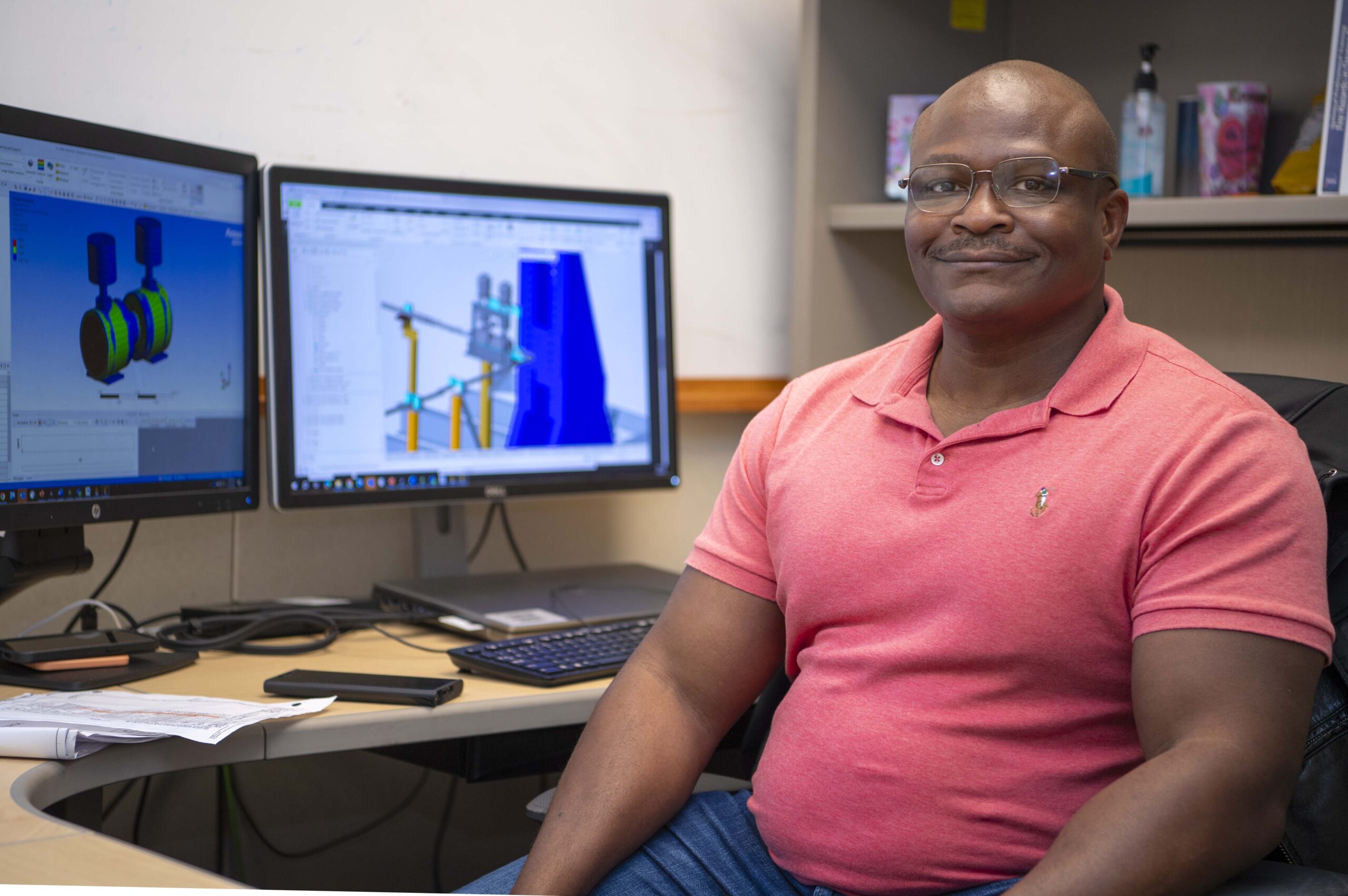 s25 012 robert williams.jpg Robert Williams, wearing a coral polo styled shirt, poses for a portrait while seated at his workstation