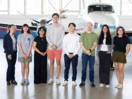 NASA’s 2025 SARP East Atmospheric Chemistry Group Announced A group of eight people stand together inside a hangar with a somewhat shiny floor. In the background is a small white plane with a blue stripe, and large windows behind that.