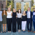 NASA’s SARP West 2024: Oceans Group Exploration A group of eight people. the first a professor and the other seven college age, stand in a line in professional attire. Behind them is a glass building with glass doors, reflecting green trees.