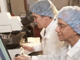 NASA Tech Prevents Heart Failure in Astronauts Image of two engineers wearing white lab coats facing left. The engineer on the right is working on a computer, and the engineer on the left is looking through a microscope.