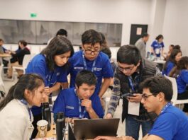 2025 NASA Space Apps Challenge Now Open for Registration Six people look at a laptop computer in a classroom setting. Four wear blue t-shirts, one wears a white jacket, and one wears a plaid shirt with a black vest.