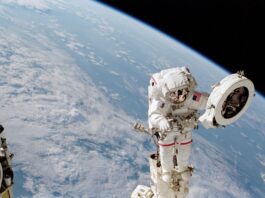 NASA: Reaching New Heights Beyond Earth An astronaut in a white spacesuit works on a fixture while outside of the International Space Station. He holds a large white circular object in his left hand. Earth can be seen behind him: the planet