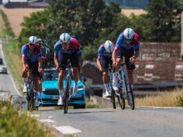 NASA Fabrics Travel through France on a Cycling Tour A team of racing cyclists clad in racing gear riding up a hill, a blue car driving behind them