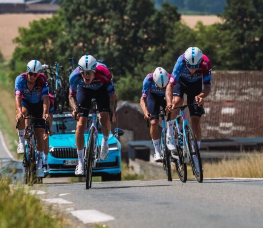 NASA Fabrics Travel through France on a Cycling Tour A team of racing cyclists clad in racing gear riding up a hill, a blue car driving behind them