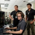 Marshall’s NASA Tools Aid Space Station Operations Three men standing inside a computer room reviewing information on a computer screen.