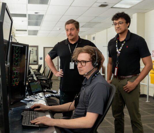 Marshall’s NASA Tools Aid Space Station Operations Three men standing inside a computer room reviewing information on a computer screen.