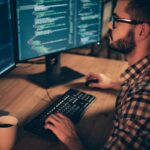 Monitoring Server Load in Linux: A Comprehensive Guide Programmer coding on dual monitors at night.