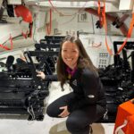 Branelle Rodriguez Prepares Orion for Artemis II Launch – NASA A woman crouches inside the mockup of a spacecraft that is equipped with seats for crewmembers.