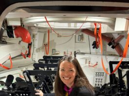 Branelle Rodriguez Prepares Orion for Artemis II Launch – NASA A woman crouches inside the mockup of a spacecraft that is equipped with seats for crewmembers.