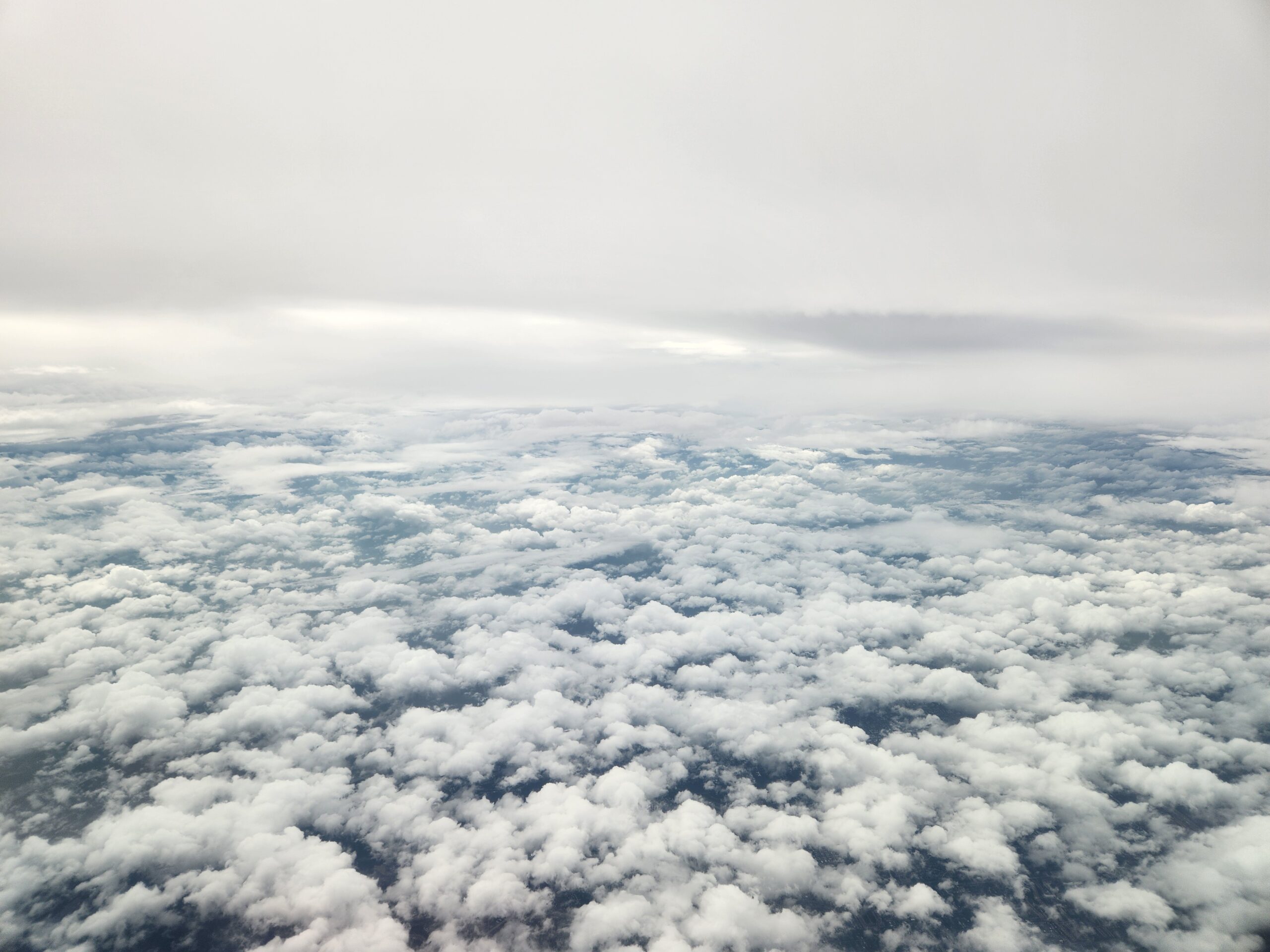The image shows an aerial view of grey skies above and thick, broken cloud cover below.